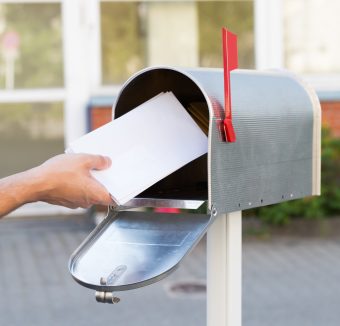 Close-up Of Person Putting Stack Of Letters In Mailbox